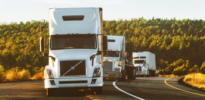 Three semi trucks driving on a highway through a forested landscape in Arizona.